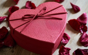 Большая красная коробка в форме сердца на столе с лепестками роз