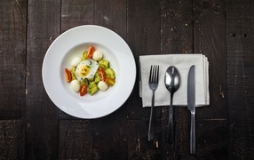 Scrambled eggs with vegetables in a white plate on a table with cutlery