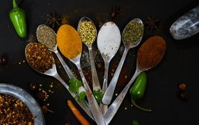 Spoons with aromatic spices on a black table
