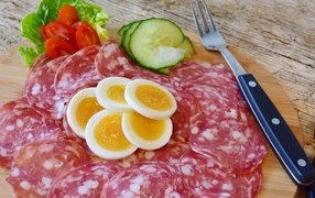 Salami sausage on a board with boiled eggs and vegetables