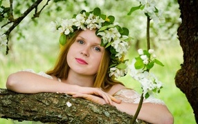 Красивая девушка с венком из цветов на голове у дерева весной