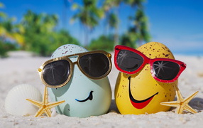 Two eggs in sunglasses on the sea sand in summer