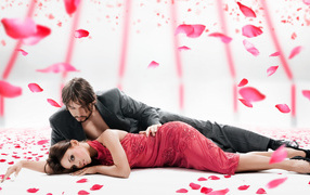 A girl in a red dress lies on the floor with a man in a suit