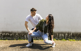 The guy and the girl are dancing on the background of a gray wall