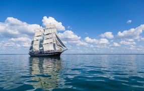 Big ship with white sails at sea under blue sky