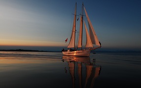 Large yacht with white sails at sunset in the sea