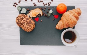 Croissant on the table with cookies, cup of coffee and tangerine