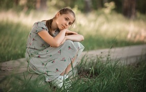 Девушка в платье сидит у зеленой травы