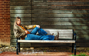Молодая девушка в синих джинсах лежит на лавке