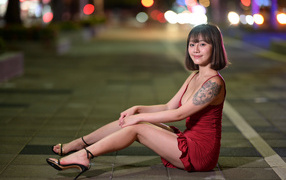 Милая азиатка в красном платье сидит на дороге