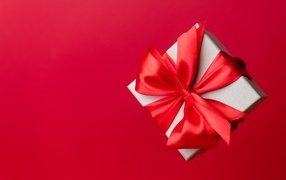 Gift with a satin ribbon bow on a red background