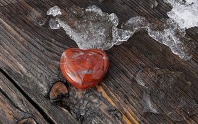 Heart made of stone on a wooden bench with melting snow