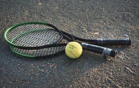Two rackets and a yellow tennis ball on the asphalt
