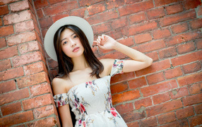 Азиатка в белой шляпе стоит у кирпичной стены