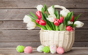 White and red tulips in a basket on a table with colorful eggs for Easter