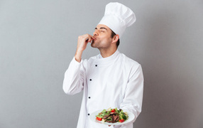 Male chef in a white suit with a dish on a gray background
