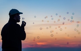 Man blowing soap bubbles at sunset