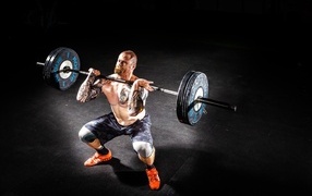 Strong man with tattoos on his body lifts a barbell