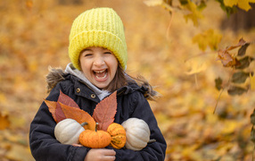 Веселая девочка с тыквами и листьями в руках осенью