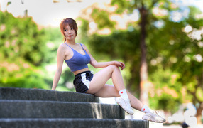 Спортивная азиатка в кроссовках сидит на ступеньках